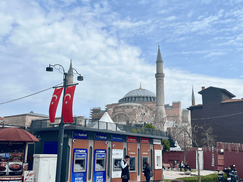Pohled na Hagia Sophia v Istanbulu s typickým ruchem ulice – bankomaty a malé občerstvení v popředí ukazují, že i u nejslavnějších památek se potkává historie s každodenním životem. (Co vidět v Istanbulu)