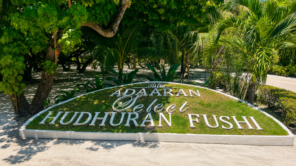 Uvítací nápis Adaaran Select Hudhuran Fushi v tropické zeleni na Maledivách.