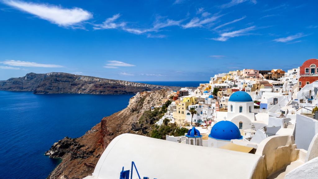 Výhled z Oie na Santorini s modrými kupolemi, bílými domy, kalderou a Egejským mořem